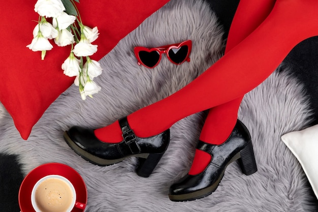 Woman's legs in fashionable shoes with sunglasses and flowers on gray furry surface