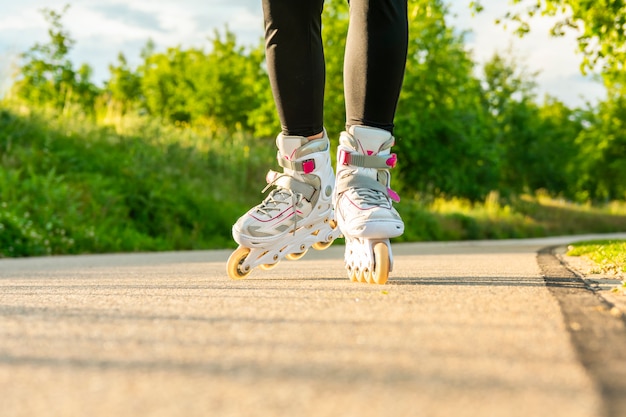 Woman's legs with white roller blades at sunny day on asphalt road.