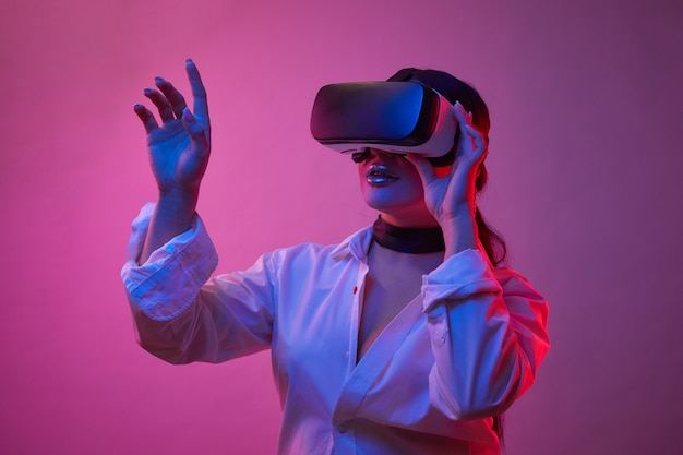 파란색 배경에 네온 불빛에 VR 안경에서 여자가 놀고 있습니다. VR 고글의 소녀는 가상 현실 경험을하면서 옵션을 선택합니다.