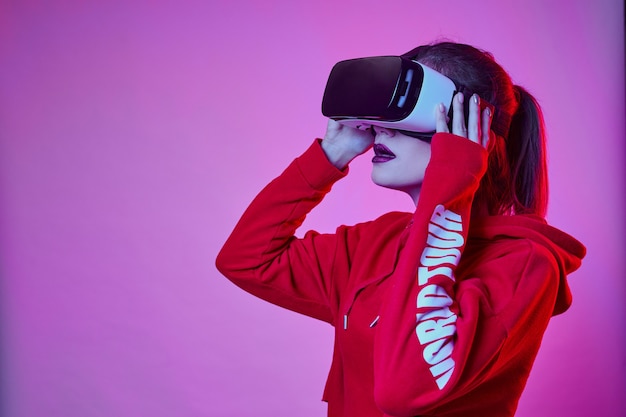 Woman's playing in VR-glasses in neon light on blue wall. Girl in VR goggles choosing options while having virtual reality experience.