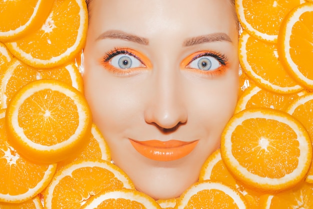 Photo woman's portrait with oranges closeup. bright orange make up