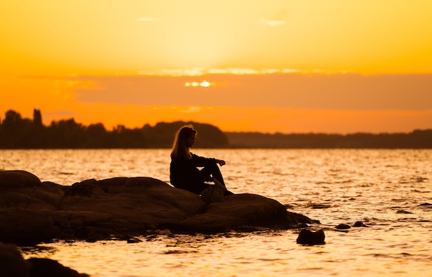 まっすぐに見える岩の上に座って日没時の女性のシルエット