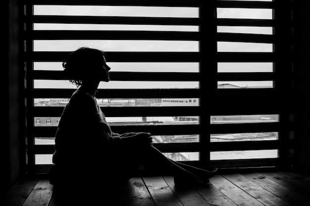 Woman's silhouette at the window of the house in winter, gentle and pensive sitting on the floor