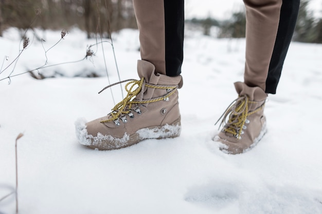 사진 여자의 세련된 겨울 갈색 따뜻한 가죽 신발. 남자는 겨울 숲을 안내합니다. 남성 다리의 클로즈업입니다.