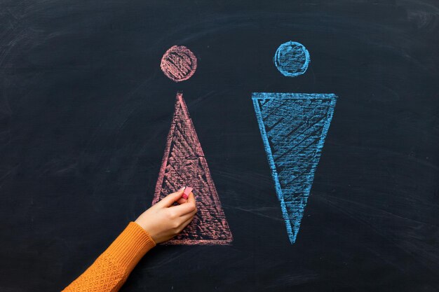 A woman's teacher's hand draws gender symbols of men and women on a chalkboard, sex education