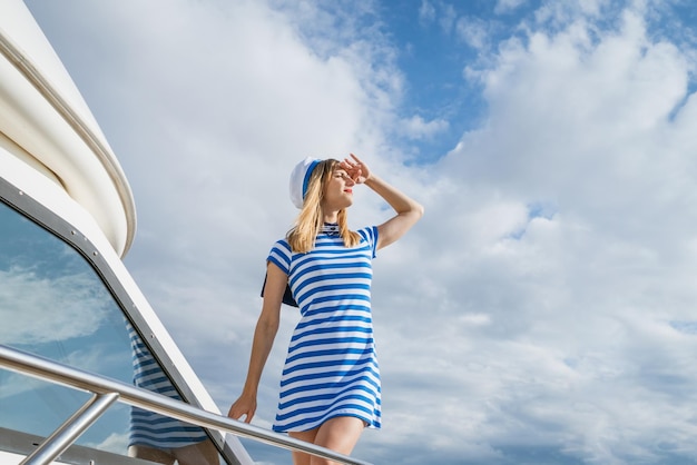 Woman sailor stands on deck yacht with striped dress and cap looks