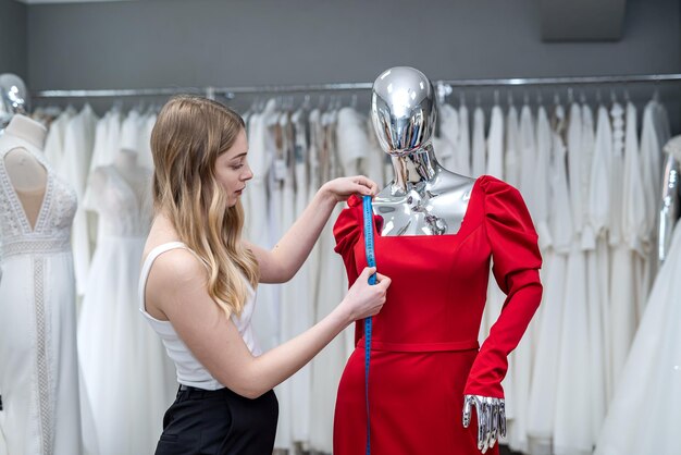 Woman saleswoman measures evening dress with tape measure in the salon