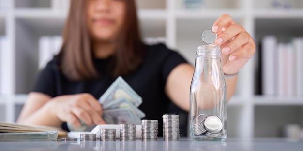 Woman saving money with hand putting coins in jug glass concept finance and accounting finance and saving money for future concept