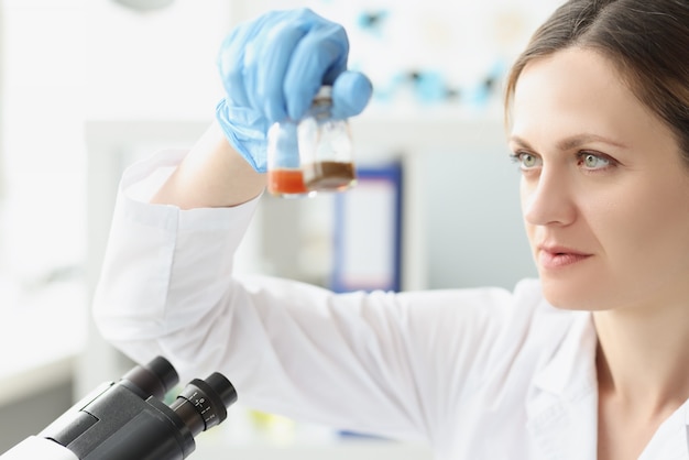 Woman scientist chemist holding glass jars with medicine in front of microscope development of