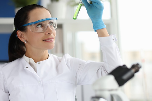 Woman scientist chemist looking at test tube with green liquid in laboratory pharmaceutical