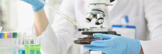 Woman scientist drips liquid oil from pipette into cup of soil laboratory study of soil concept