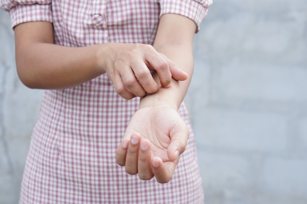 Woman scratching arm from itching on  gray background
