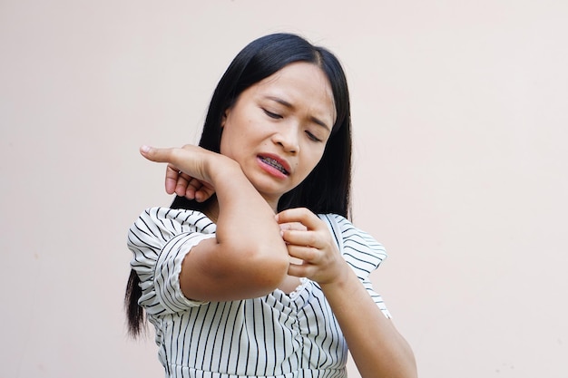 Woman scratching arm from itching on light gray background\
cause of itchy skin include insect bites