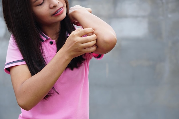 Woman scratching arm from itching on light gray background\
cause of itchy skin include insect bitesconcept of health care\
skin