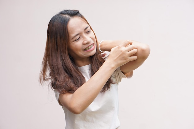 Woman scratching arm from itching on light gray background Cause of itchy skin include insect bitesConcept of health care skin