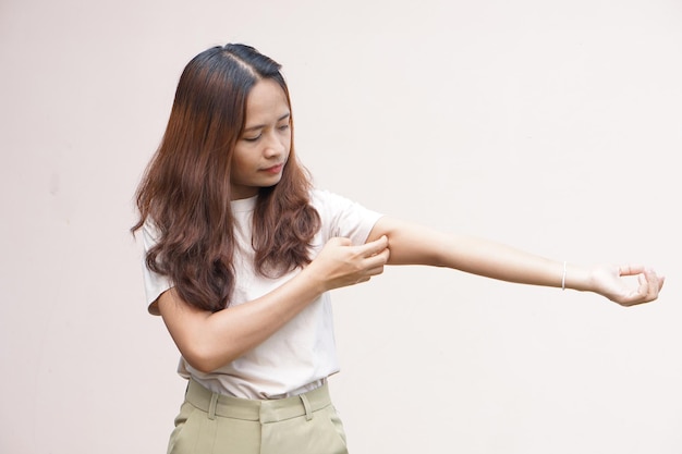 Woman scratching arm from itching on light gray background Cause of itchy skin include insect bitesConcept of health care skin