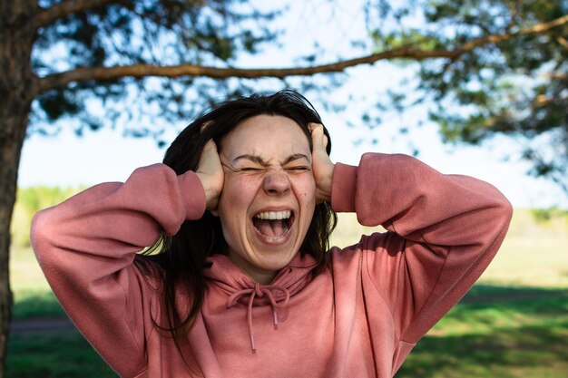 Foto la donna urla forte, spalancando la bocca, chiudendo gli occhi e tenendosi la testa tra le mani