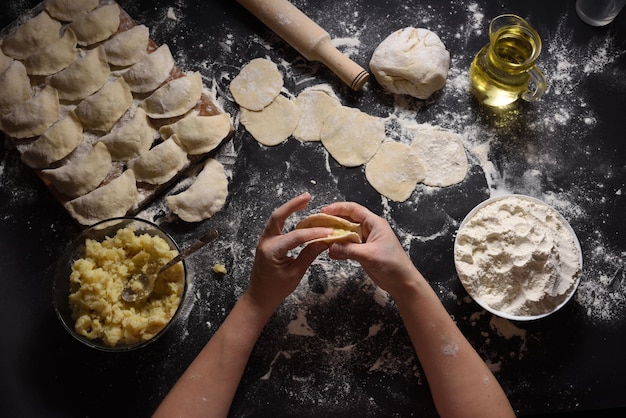 Woman sculpts dumplings with handmade potatoes on a black background Shot from the top angle Ukrainian folk cuisine