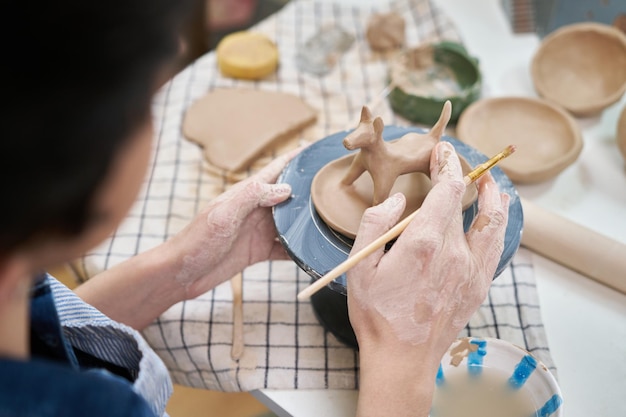 Woman sculpts a figurine of a dog from clay by hands closeup in artistic studio