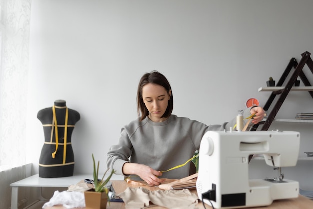 A woman seamstress in the background of her working workshop is engaged in sewing clothes