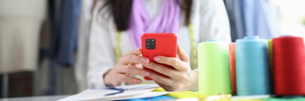 Woman seamstress stylist holding smartphone in atelier