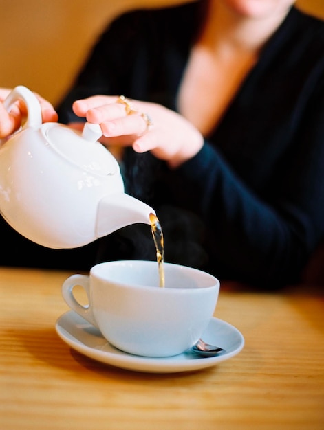 A woman seated pouring a cup of tea out of a white china tea pot