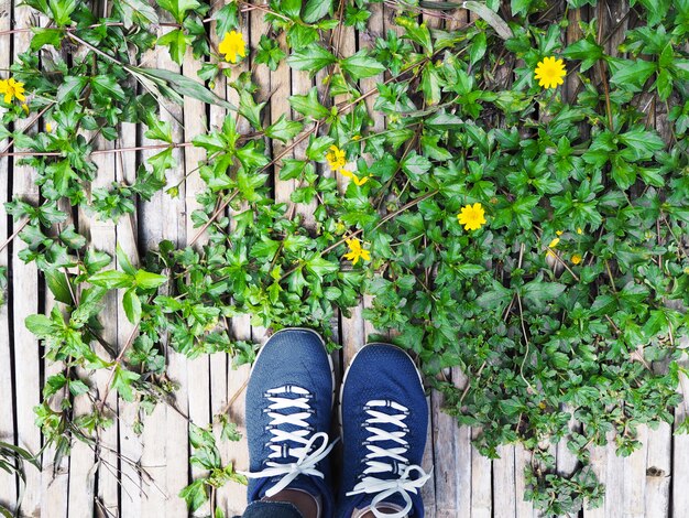 Woman selfie feet on wooden footpath with green creeper plant and small yellow flowers.