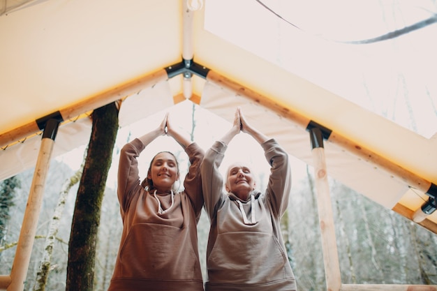 Donna anziana e giovane rilassante al glamping tenda da campeggio donne famiglia anziana madre e giovane figlia facendo yoga e meditazione indoor moderno concetto di stile di vita vacanza zenlike