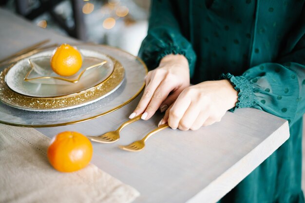 Una donna serve una tavola festiva. forchette e piatti d'oro, mandarini