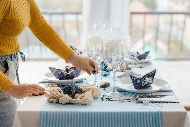 Woman serving party table in blue colors with textile tablecloth, white dishes, glasses for wine and golden cutlery. birthday decoration. close up