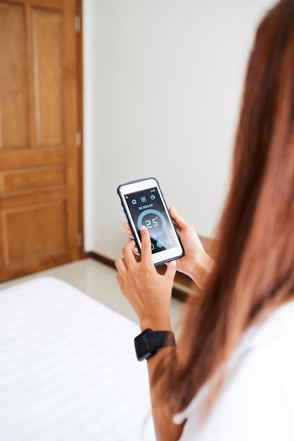 Woman setting temperature in bedroom via smart home application on her smartphone