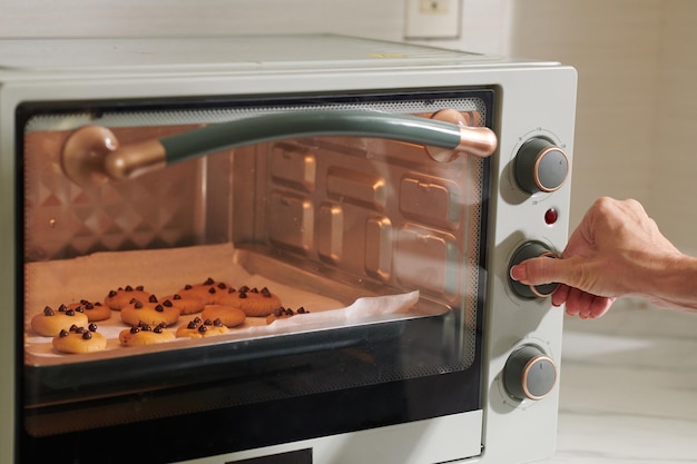 Woman setting time and temperature on oven when baking cookies