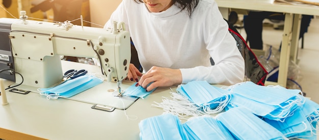 Woman sew the facial medical at sewing machine. Coronavirus pandemia.