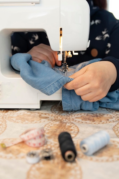 Una donna che cuce e ripara i vestiti con una macchina da cucire a casa