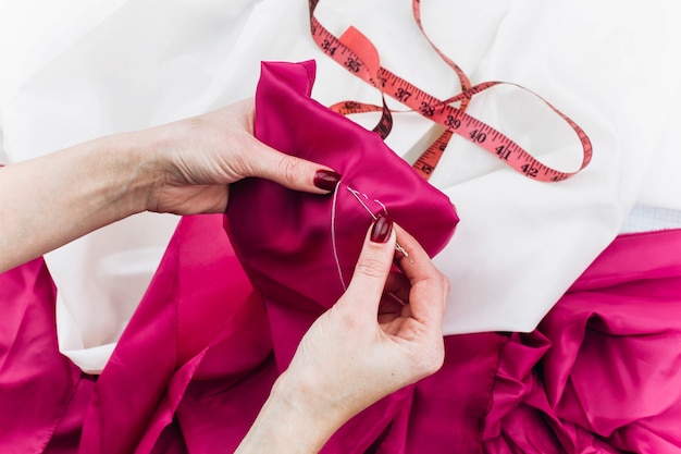 Woman sews dark pink cloth on the table 