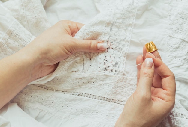 Woman sews a dress. Hands with a needle and thimble close up