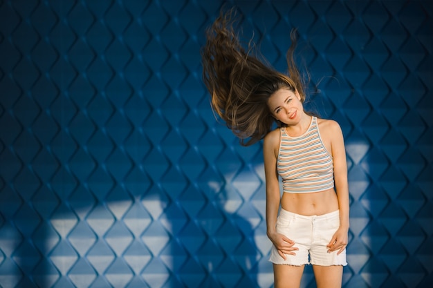 Woman shakes her hair posing before a blue wall