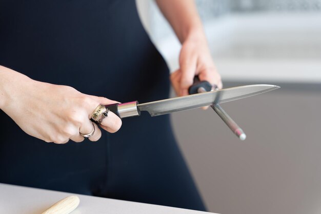 Woman sharpening a knife with a grinder, close-up view with blurred horizontal background