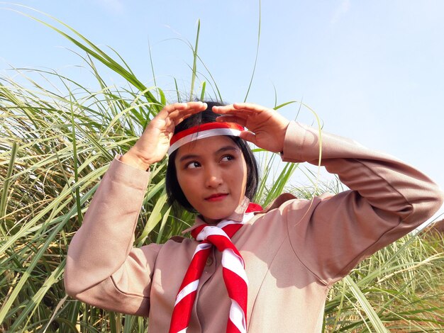 Woman shielding eyes by plant against sky