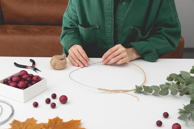 셔츠를 입은 여성이 나뭇잎으로 만든 장식용 가을 화환을 만들기 위해 공작물을 만들고 있다
