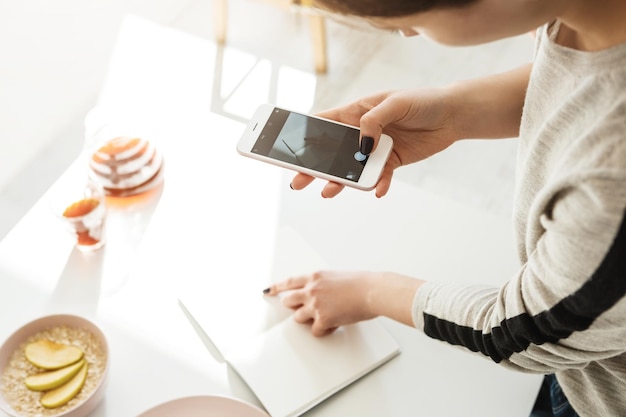 Woman shooting empty notebook with contrast lighting while having breakfast