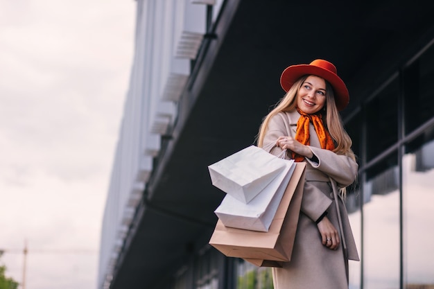 モダンな建物の近くを歩く買い物用の紙袋を持った買い物中毒の女性