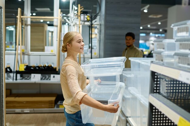 家庭用品店でプラスチック製の貯蔵容器を選ぶ女性の買い物客。ショッピングと小売