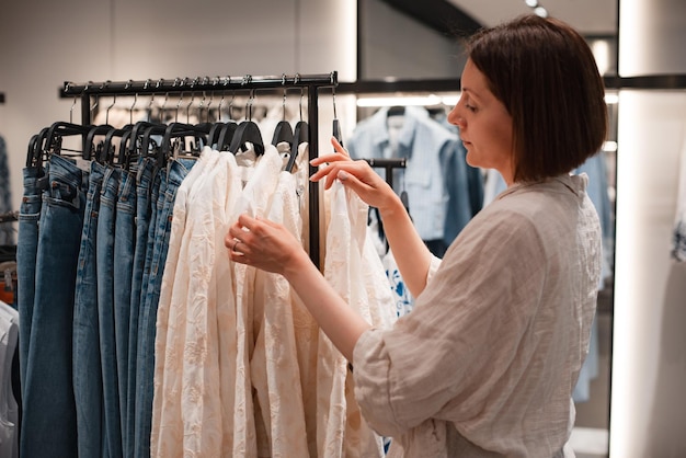 쇼핑하는 여성은 옷가게의 옷걸이에 매달려 있는 에코스타일의 세련된 자연 색상의 옷을 선택합니다. 청바지 파스텔 색상 느슨한 핏