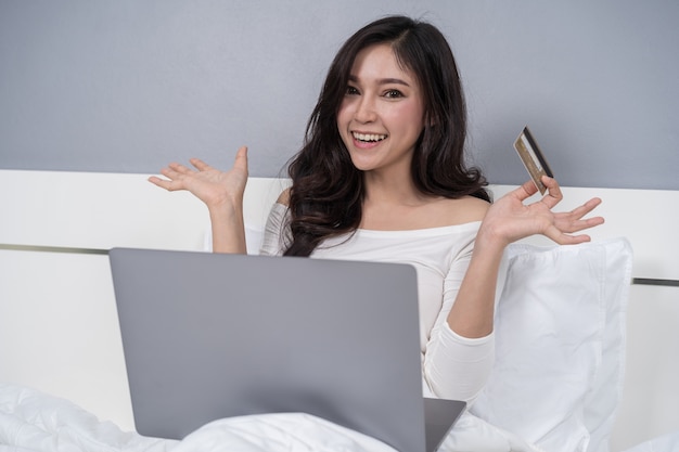 Woman shopping online with credit card and laptop computer on bed 