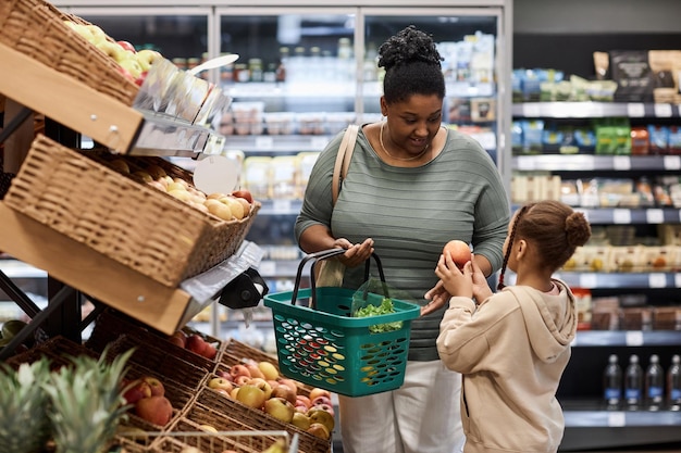 Woman shopping in supermarket with little daughter and buying fresh vegetables