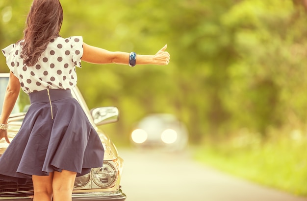 Woman in short skirt hitchhikes approaching car standing next to her broken down vintage vehicle.