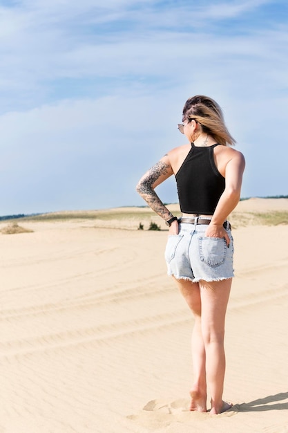 Woman in shorts in a sandy desert with hands in back pockets, rear view