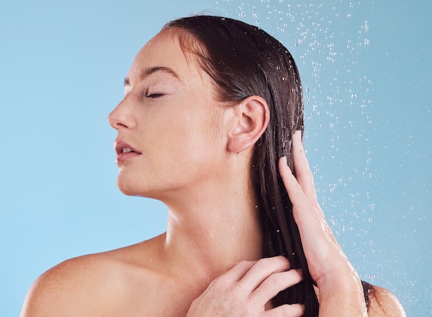 Woman shower and hair care with water studio and cleaning for hygiene beauty and health by blue background Girl young model and shampoo with wellness growth and splash for shine with cosmetics