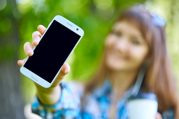 Photo woman showing blank phone screen and gadget accessories in park